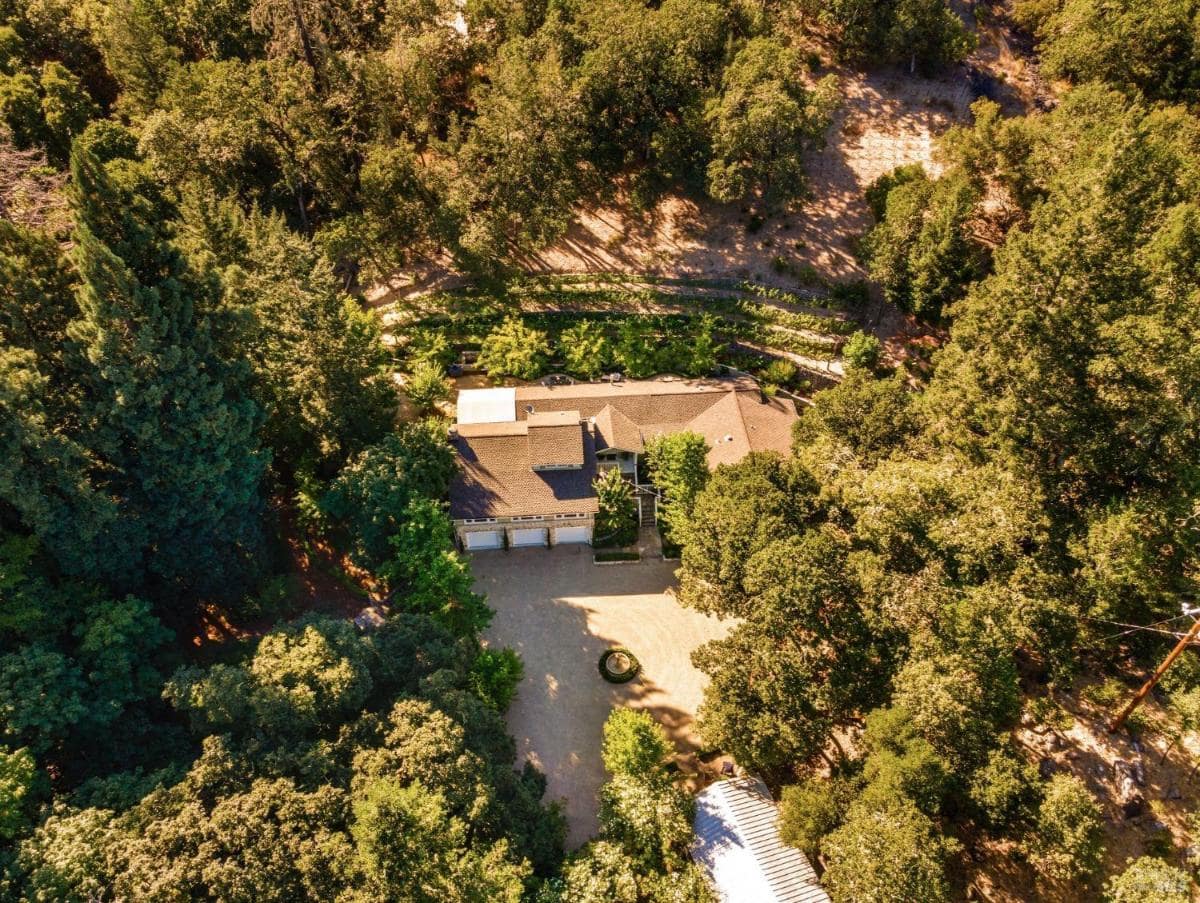 An aerial view of a house surrounded by trees and a circular driveway.

