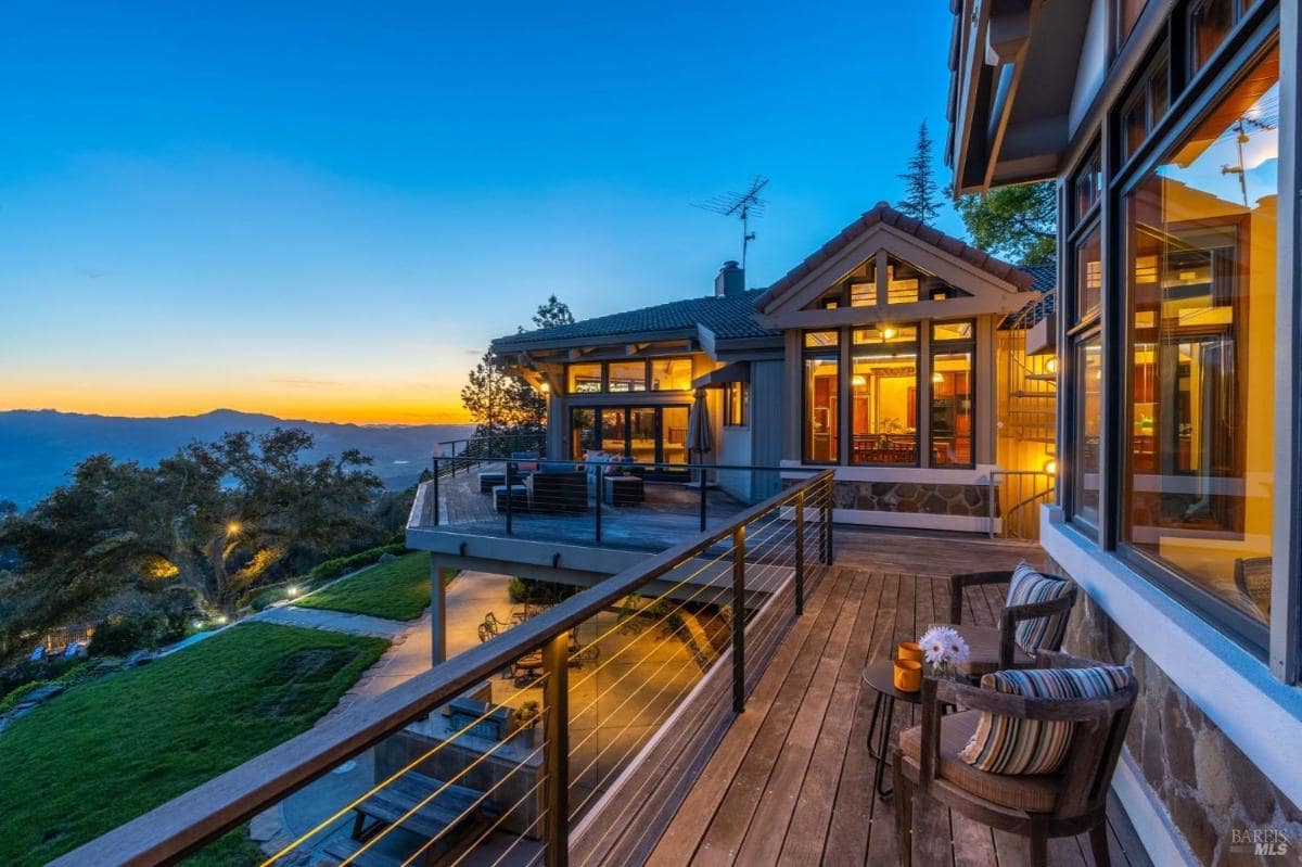 Wooden deck with outdoor seating and a view of the home at dusk.