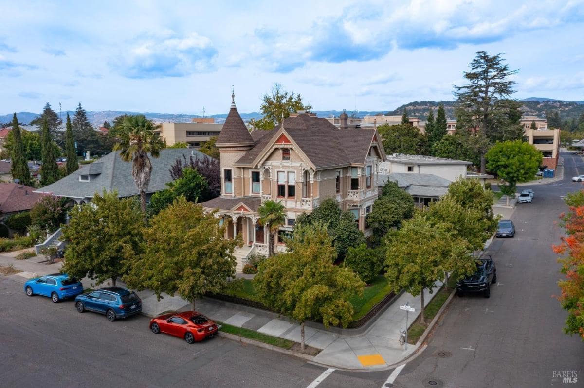 Aerial view of a Victorian-style house on a corner lot surrounded by trees.