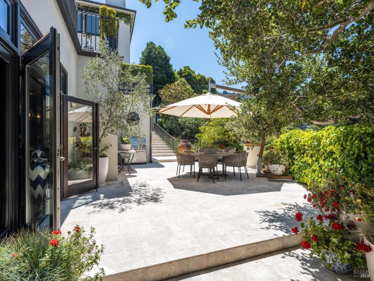 A patio dining area with an umbrella and surrounding plants.