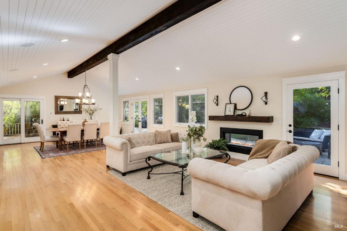 A living room features two sofas facing a coffee table, with a fireplace and windows providing natural light.

