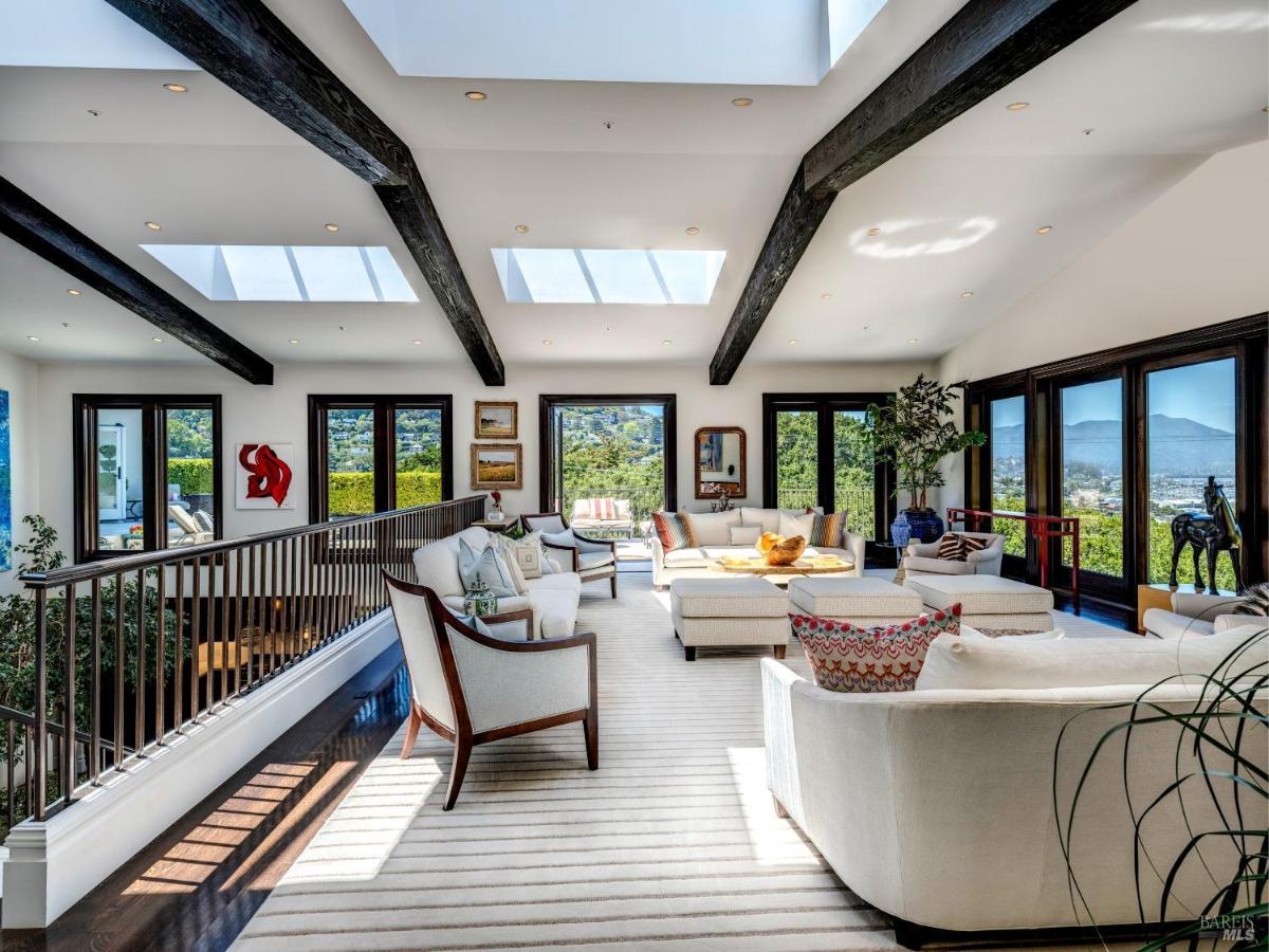 Living room with exposed beams, skylights, and large windows overlooking greenery.