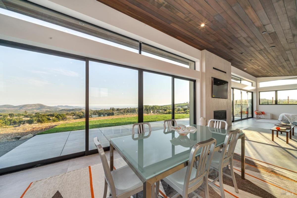 A dining area with a glass table and large windows showcasing panoramic outdoor views.