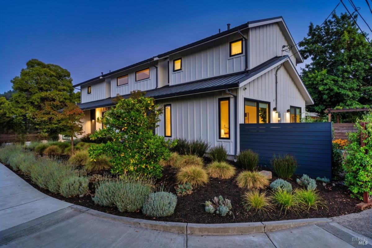 Side angle of the house during dusk with illuminated windows and landscaped greenery.