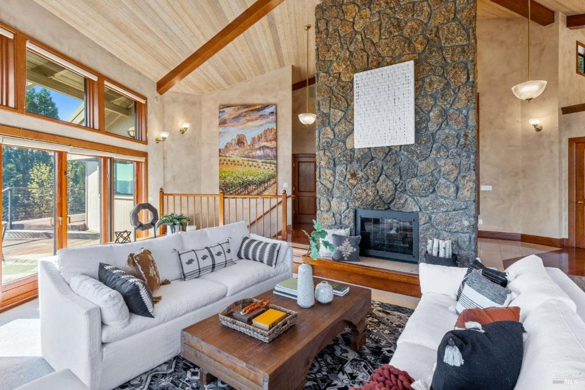 A living room with vaulted ceilings, stone fireplace, and large windows.