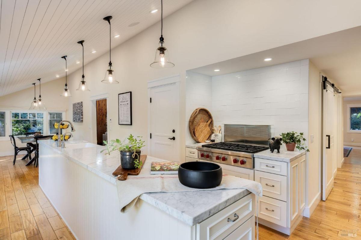 A modern kitchen featuring a marble countertop, gas stove, and pendant lighting.

