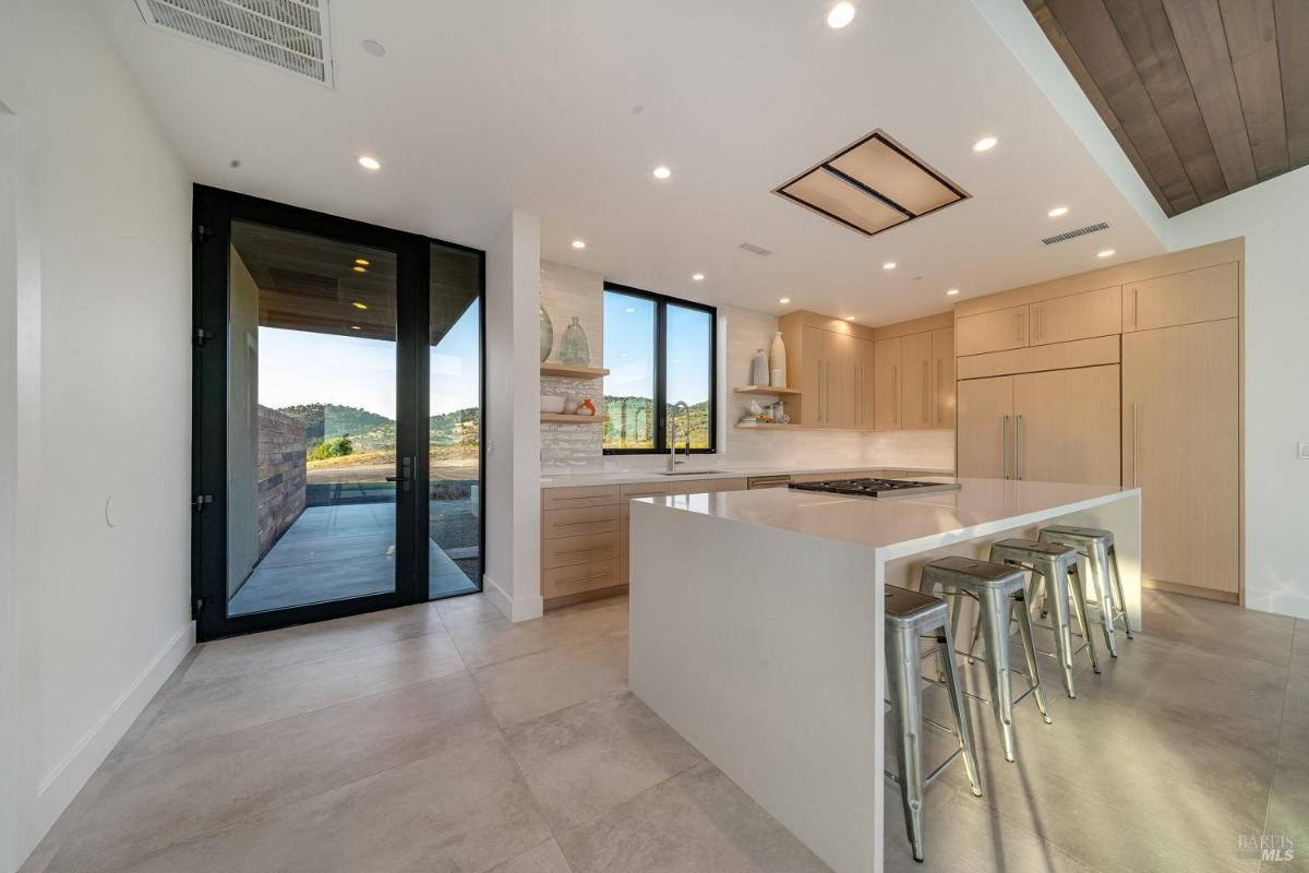 A kitchen view with open shelving, a built-in refrigerator, and large windows.