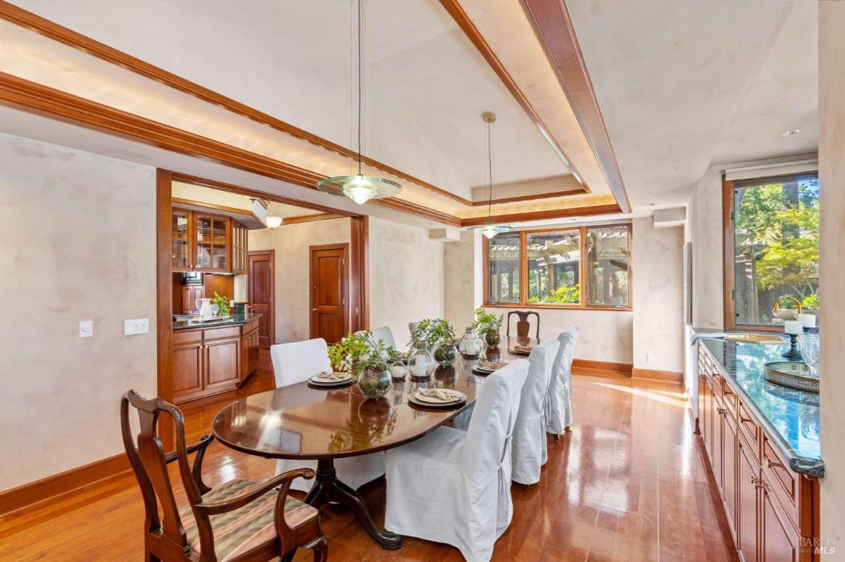 A dining room with a wooden table and chairs near large windows.