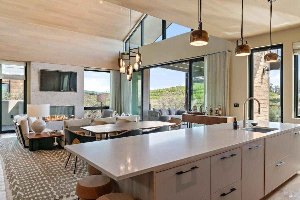 A view of a dining and kitchen space with a large central island and pendant lights.