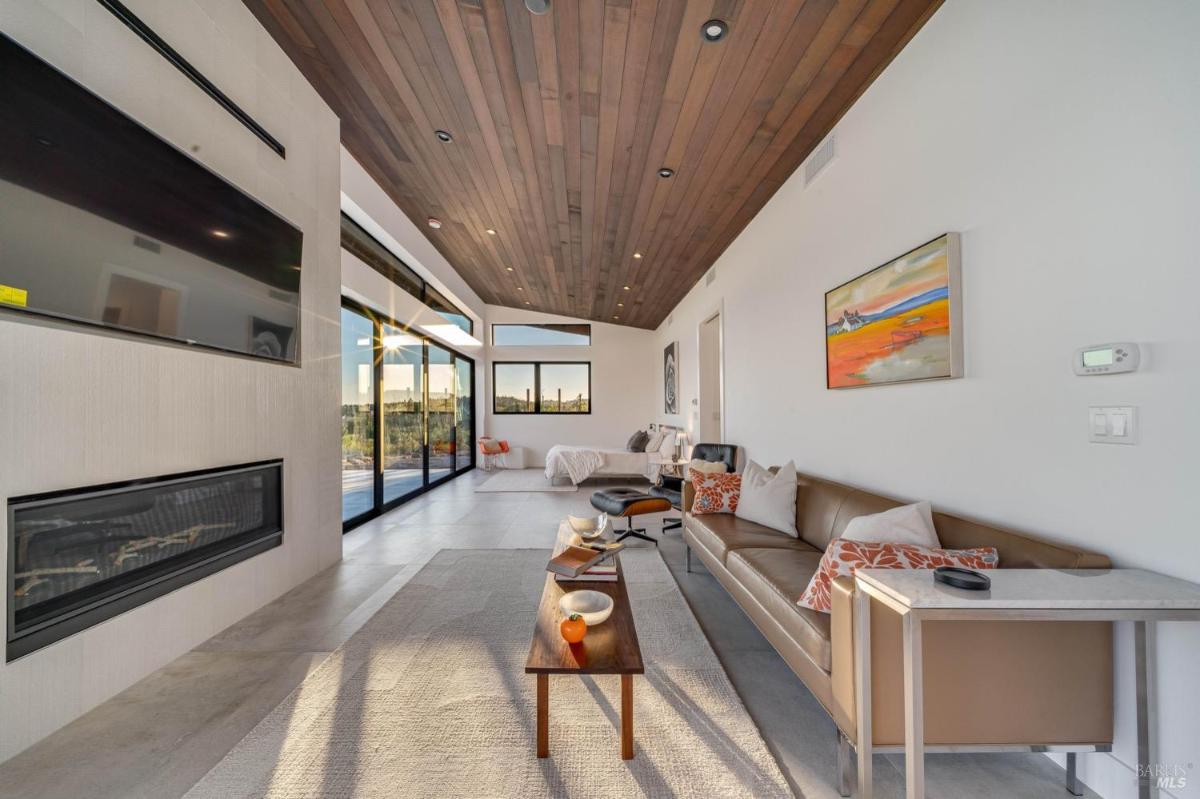 A living area with a sofa, wall-mounted TV, and access to the outdoors through sliding glass doors.