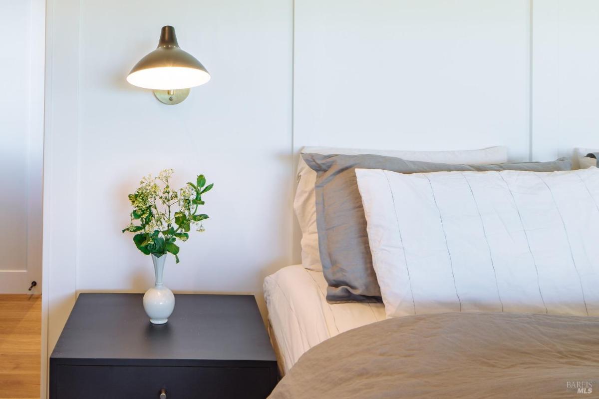 Bedroom with bedside table with a lamp and a vase holding green plants.