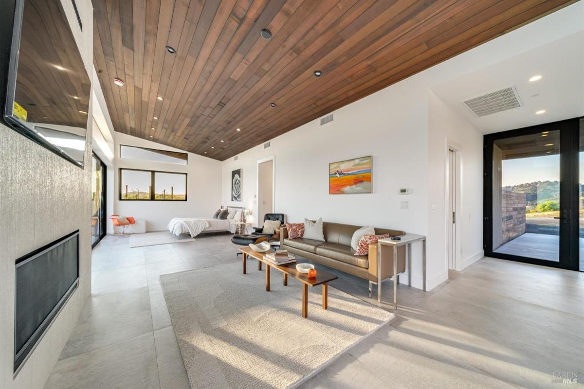 A living area with a sofa, wall-mounted TV, and access to the outdoors through sliding glass doors.