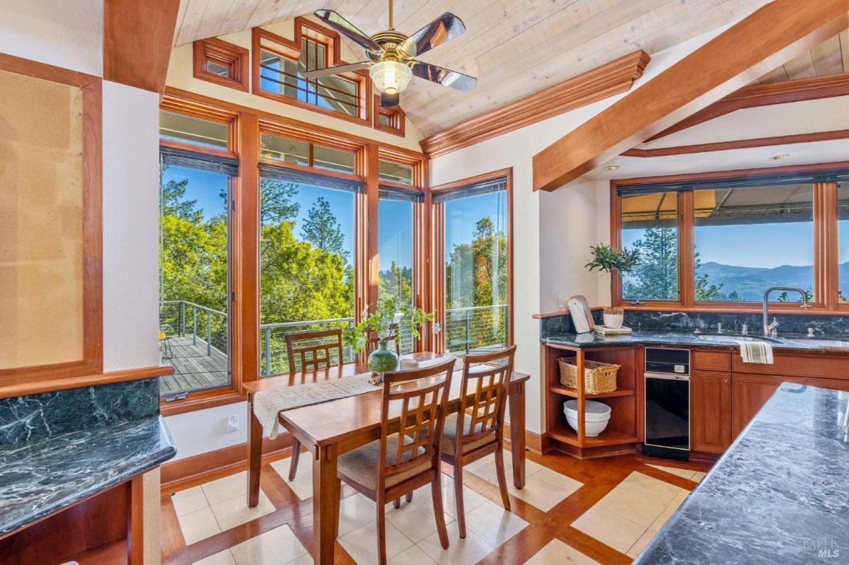 Breakfast area with wooden table and large windows overlooking trees.