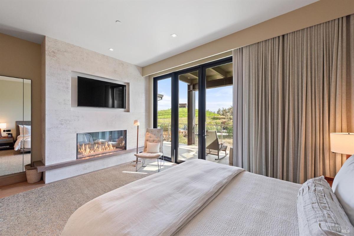 A master bedroom with a fireplace, large windows, and access to a private balcony.