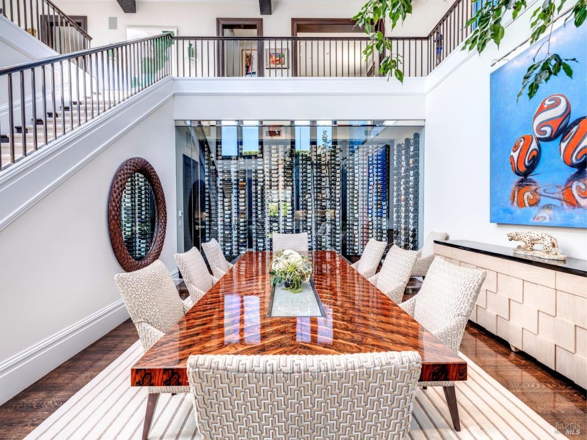 Dining table surrounded by chairs in front of a floor-to-ceiling wine storage wall.