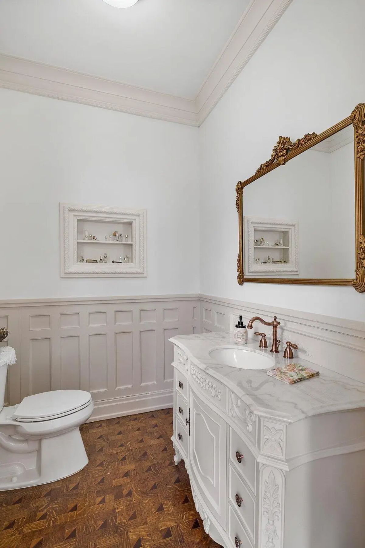 Sophisticated powder room featuring intricate wainscoting and a carved white vanity with marble countertop.