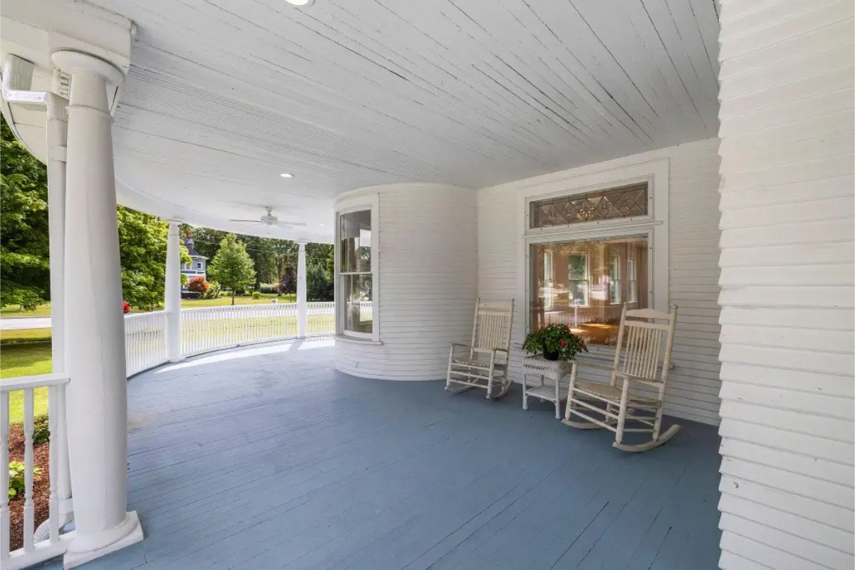 A charming wraparound porch with a smooth blue floor and white-painted woodwork offers a welcoming outdoor space.