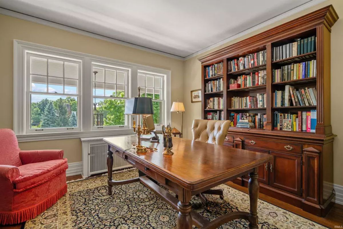 Spacious home office with a large wooden desk and built-in bookshelves filled with books. 