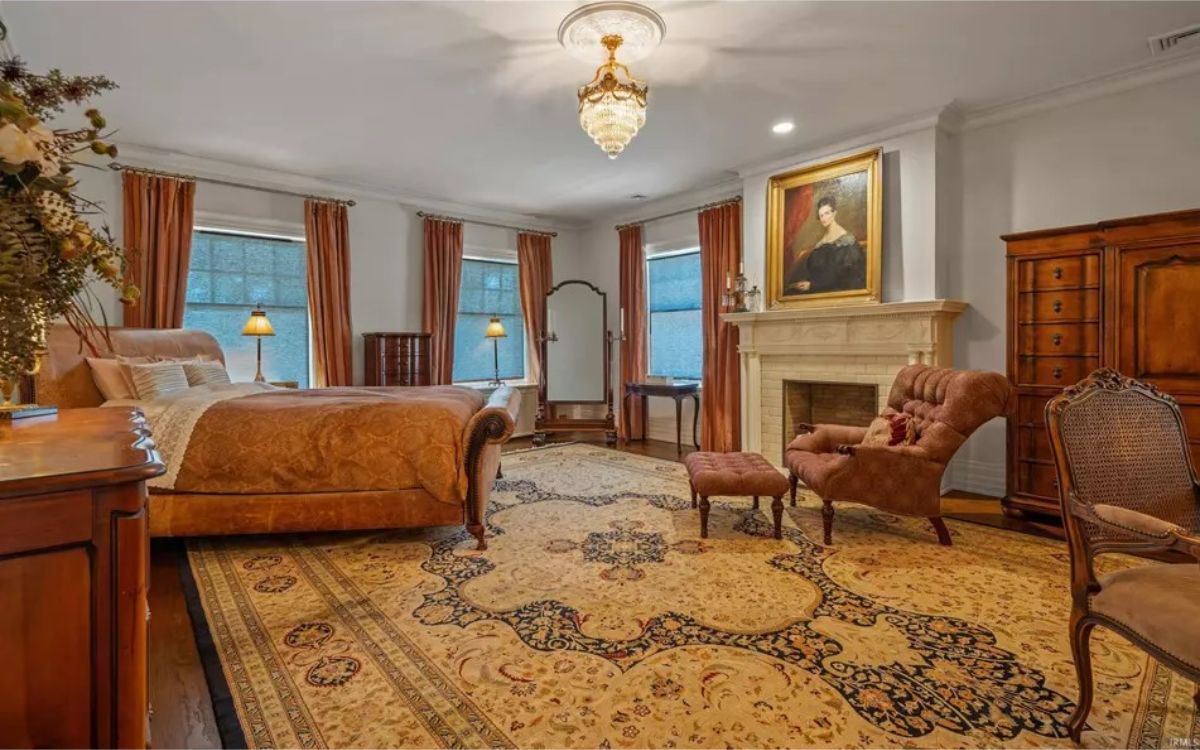 Large bedroom with a central fireplace featuring a classic mantle and portrait above. 