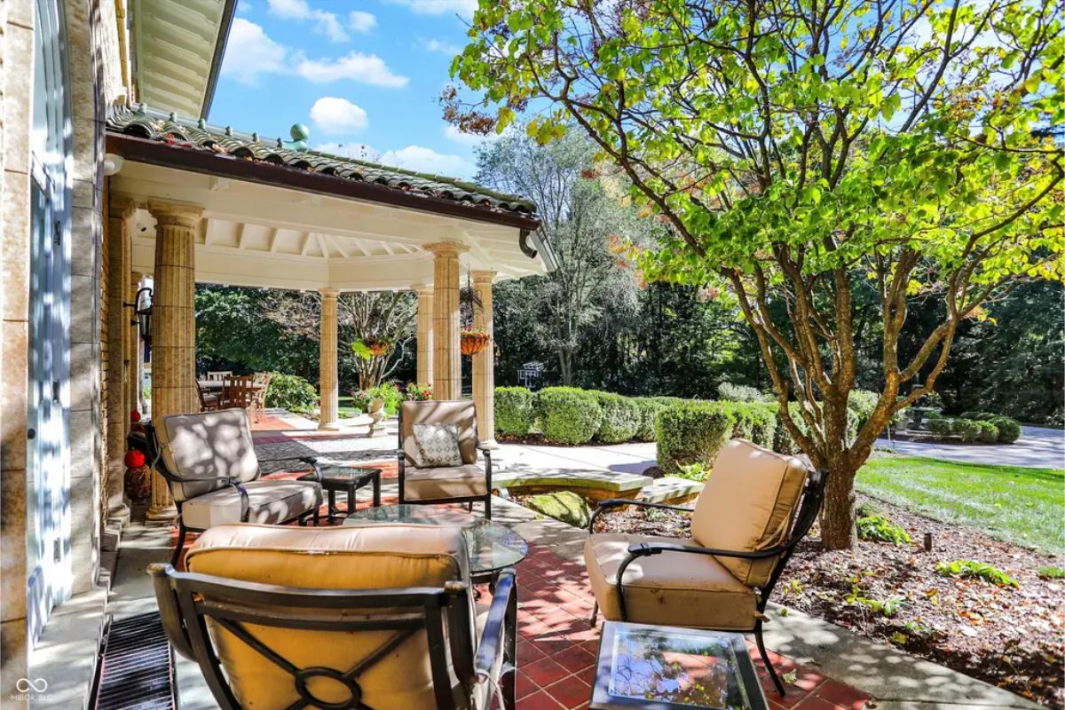 Outdoor seating area with cushioned chairs and a glass-top table on a tiled patio. 