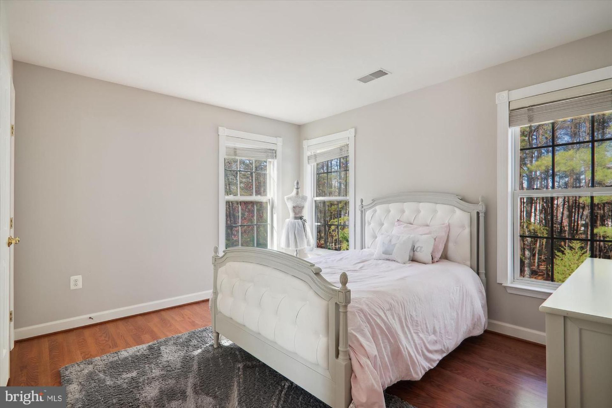 Bedroom with a white bed, wood floors, and windows overlooking trees.