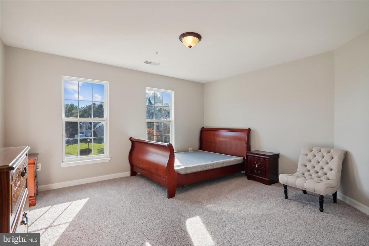 Bedroom with a sleigh bed, nightstand, and armchair. The room has neutral walls and carpeted floors.