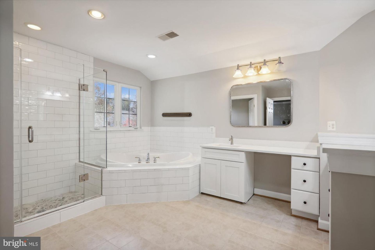 Large bathroom with a soaking tub, walk-in shower, and double vanity. The room has white subway tile and light beige floors.