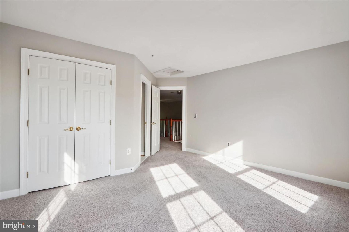 Empty room with gray carpeting, double doors to a closet, and a doorway leading to another room. Sunlight streams in through unseen windows.