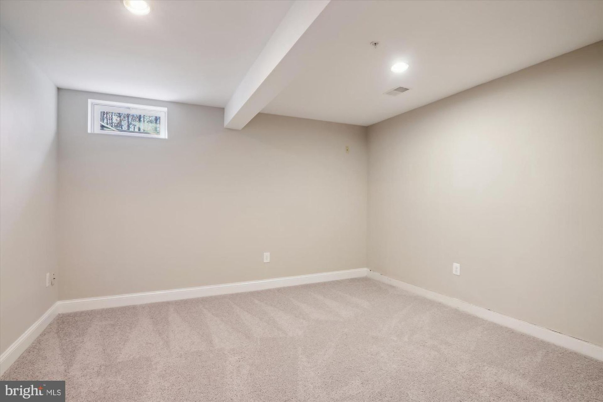 Empty basement room with gray carpeting and a single window. The walls are a light neutral color.