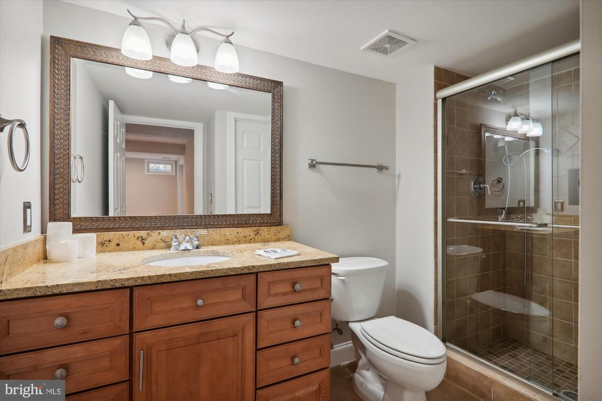 Bathroom with a wood vanity, granite countertop, and a glass-enclosed shower. There is also a toilet and a large mirror.