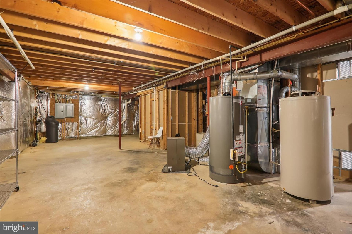 Unfinished basement with exposed wooden beams, a water heater, and other mechanical equipment. There is also a metal shelving unit.