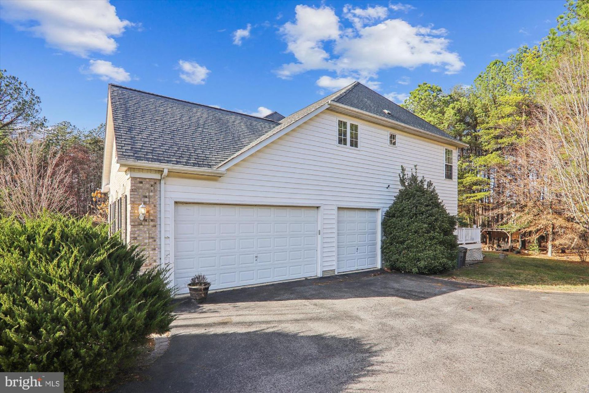 Two-car garage attached to a house. The house is light-colored with a dark roof. The garage doors are white. There is a small shrub in front of the garage.