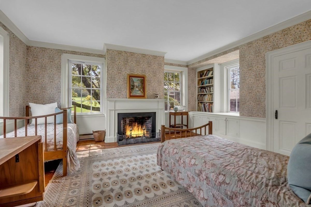 Bright bedroom with twin beds, built-in shelving, and a fireplace.