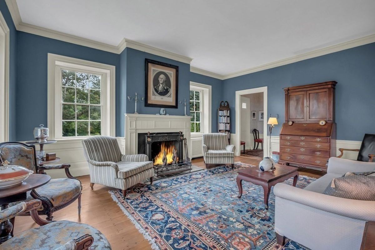 A formal room features blue walls, hardwood floors, a fireplace, and period furniture.