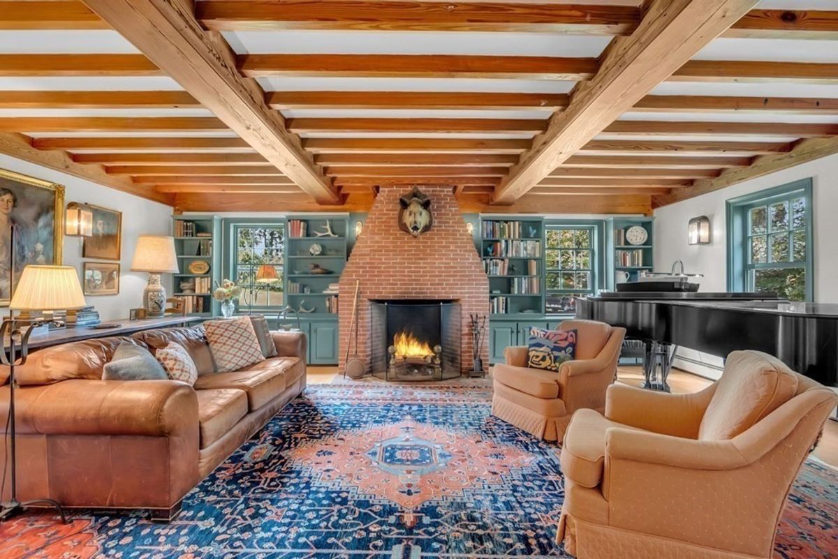 A large room features a wood-beamed ceiling, brick fireplace, and ample seating.