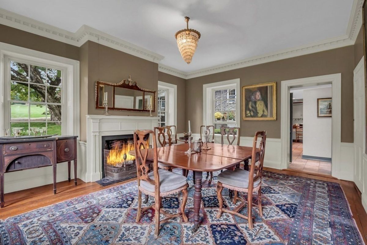 A formal dining room features a patterned rug, wood table and chairs, and a fireplace.