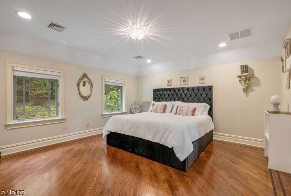 Sunlit bedroom features hardwood floors, elegant lighting, and serene forest views.