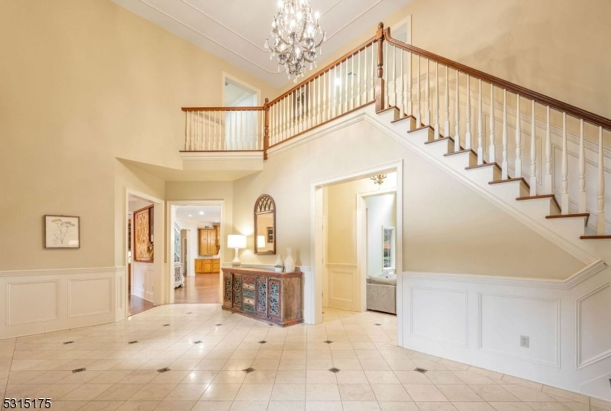 Chandelier graces the two-story foyer with an elegant staircase and polished tile flooring.