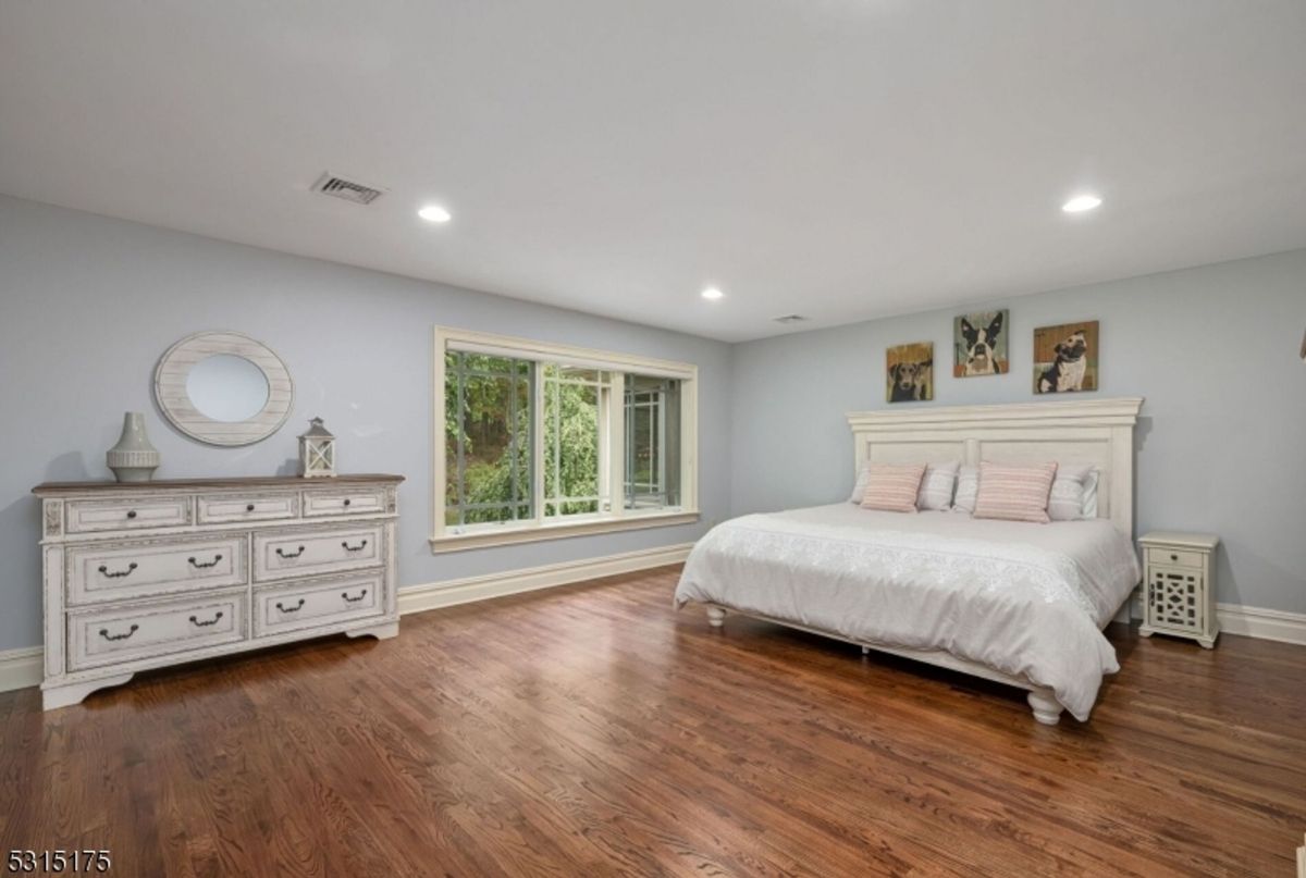 Spacious bedroom showcases hardwood floors, calming gray walls, and large windows with garden views.