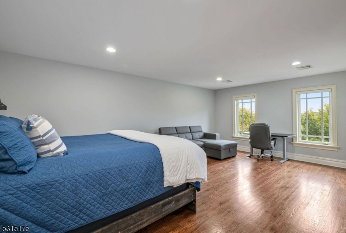 Expansive bedroom offers a cozy sleeping area, lounge space with a modern sofa, and natural light streaming through large windows.