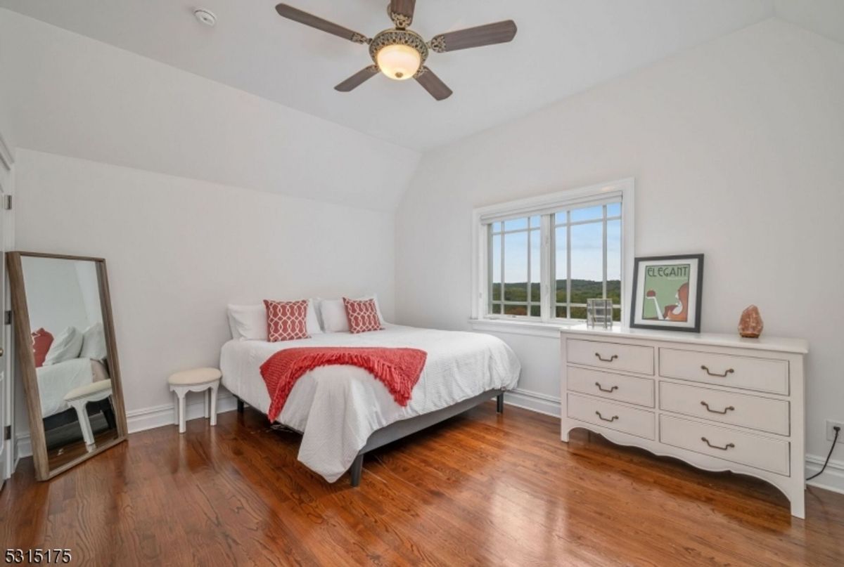 Bedroom features a clean aesthetic, natural light, and a charming view.