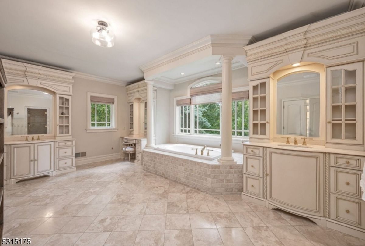 Luxurious spa-like bathroom features dual vanities, a soaking tub framed by elegant columns, and serene garden views.