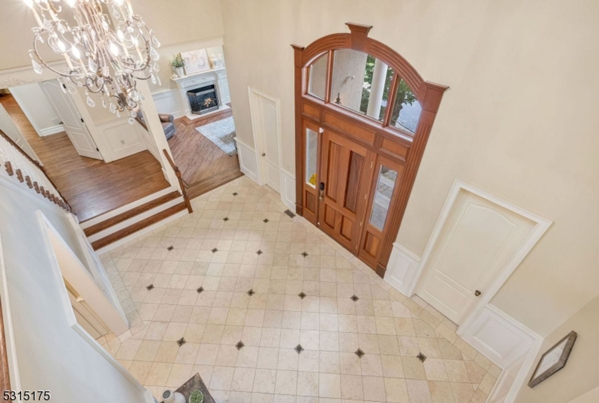 Grand chandelier illuminates the double-height foyer, complemented by detailed woodwork and elegant tile accents.