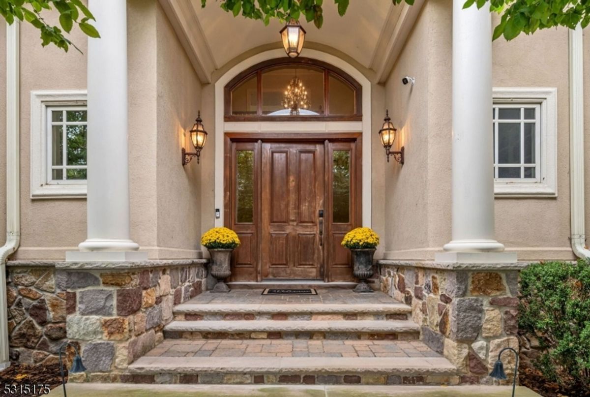 Elegant entrance features a grand wooden door framed by stonework and columns.