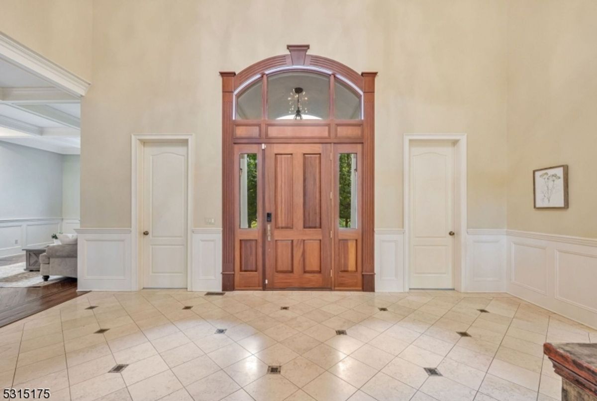 Custom wood double doors with an arched transom anchor the entryway, framed by crisp wainscoting and neutral tones.