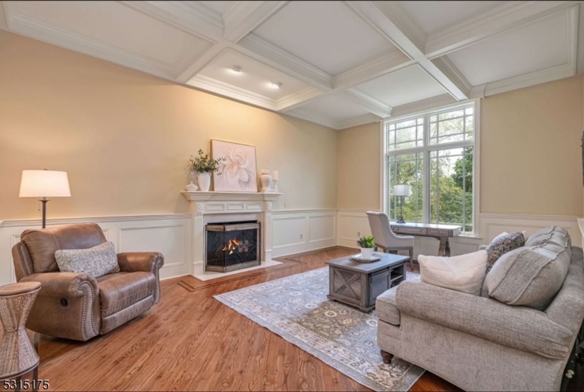 An inviting living room showcases coffered ceilings, a cozy fireplace, and an oversized window with tranquil outdoor views.