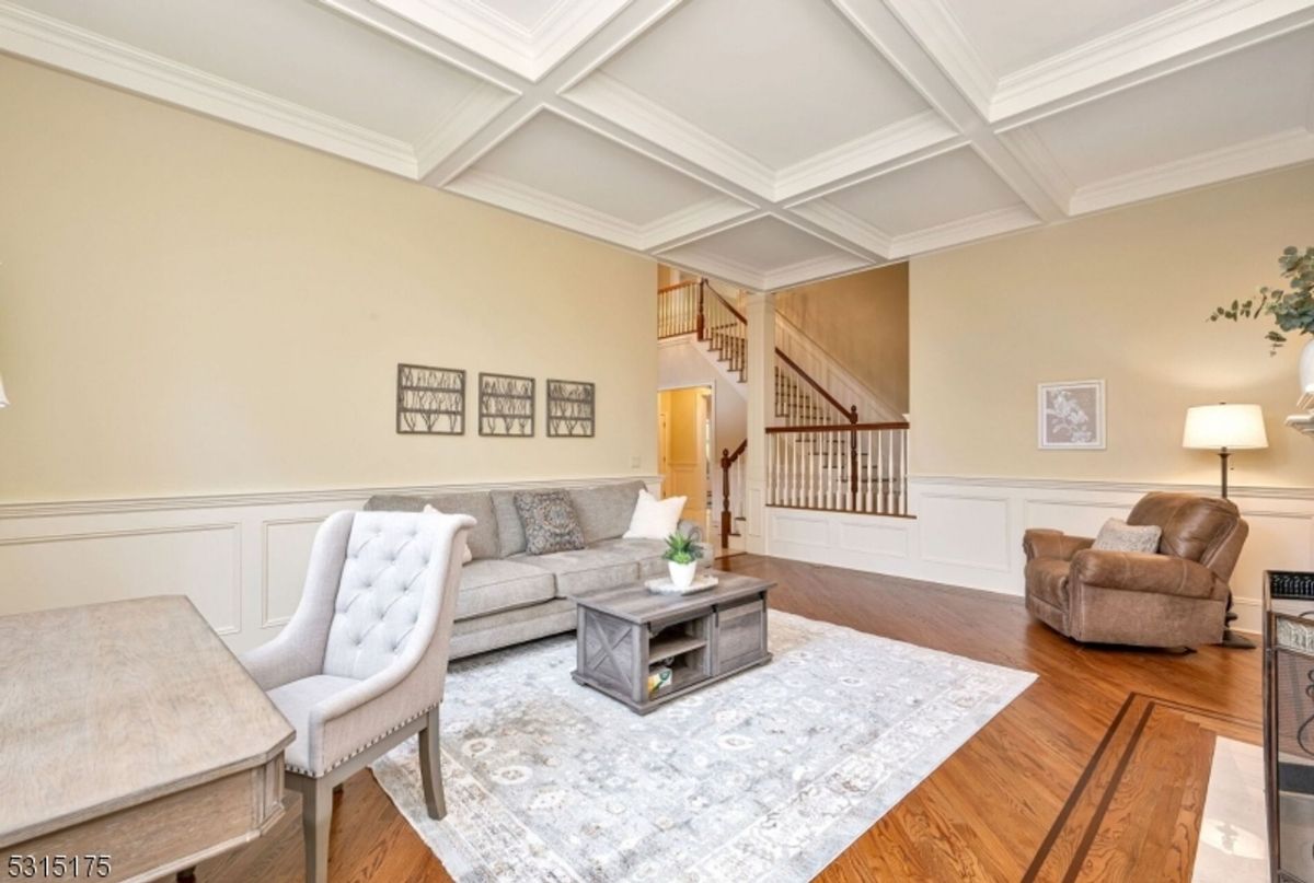 A sophisticated living room features coffered ceilings, elegant wall paneling, and seamless flow to the staircase.