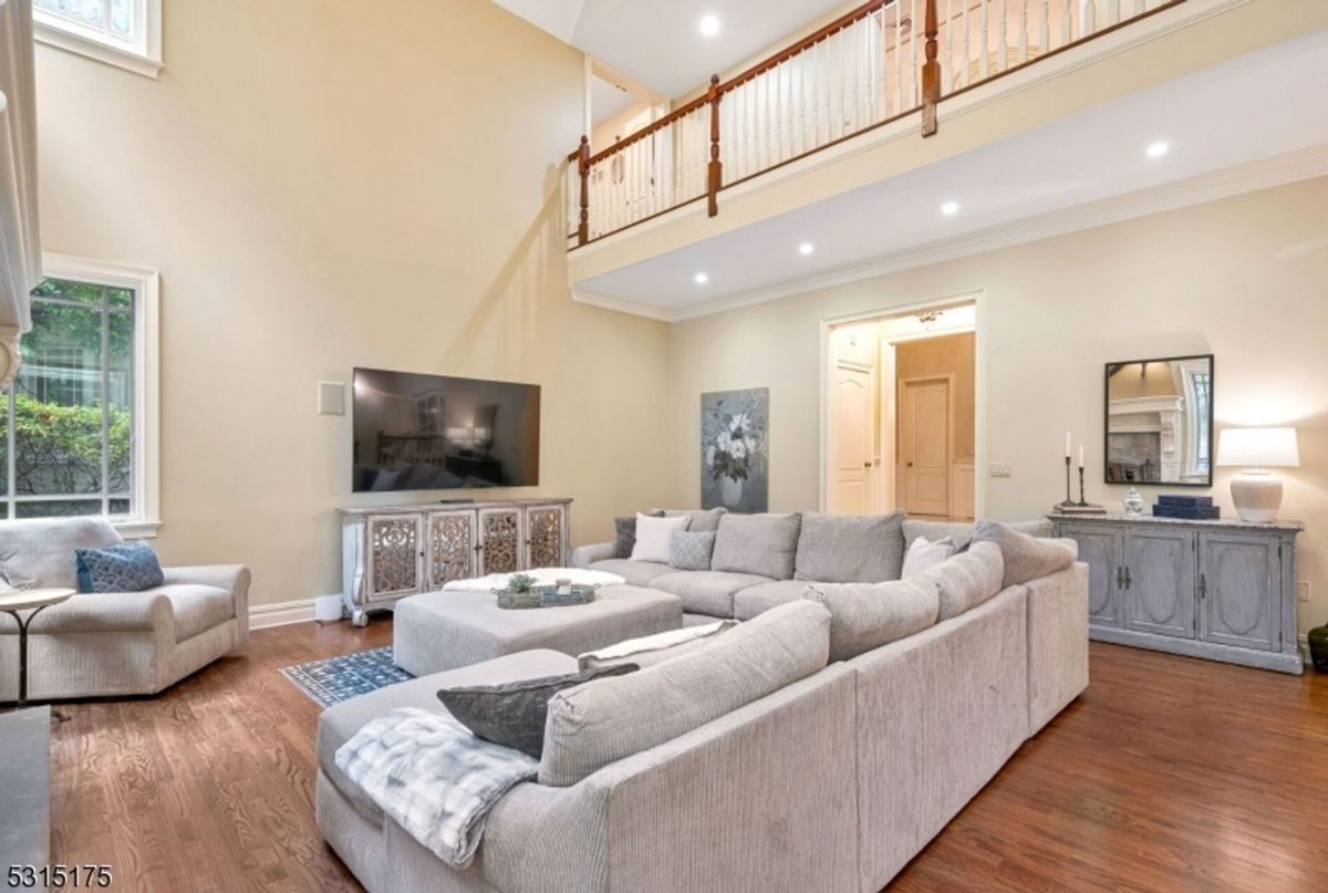 A spacious family room features a plush sectional, a large TV, and a balcony overlooking the area, creating a comfortable and stylish gathering space.