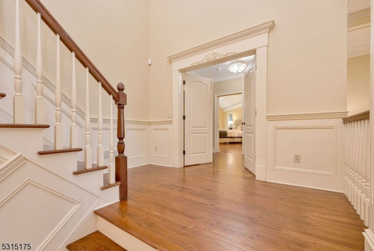 Elegant staircase features detailed wainscoting and leads to a welcoming hallway with double doors.