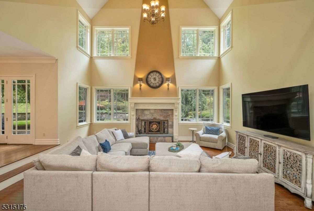 Family room features a towering fireplace, double-height ceilings, and large windows overlooking lush greenery.